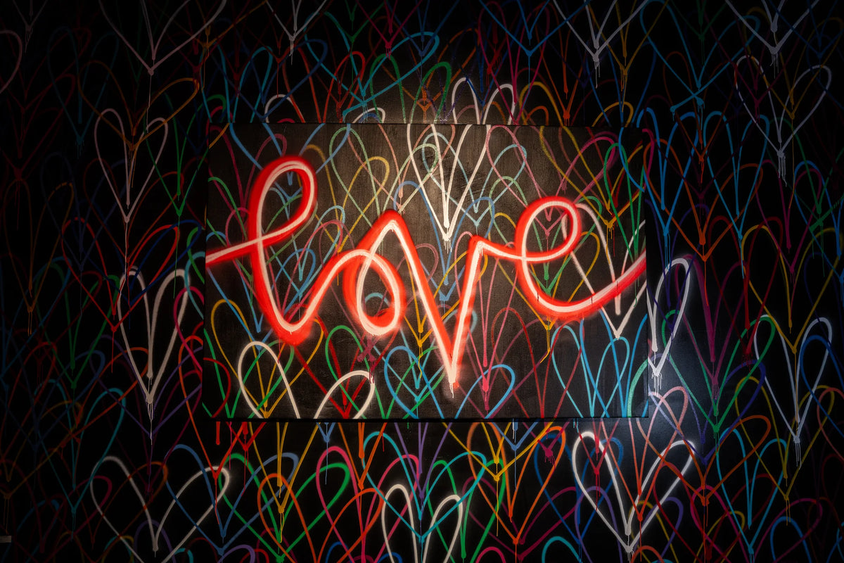 Red love neon mounted over a wall of multicolored painted hearts