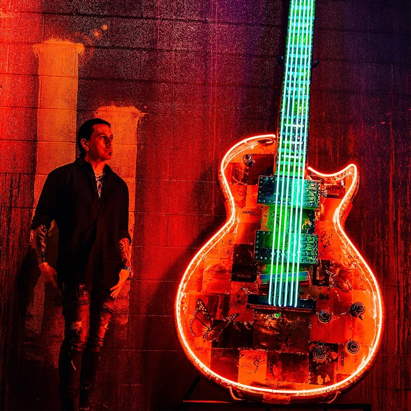 Visitor beside an oversized neon guitar at Gallery DeFi.
