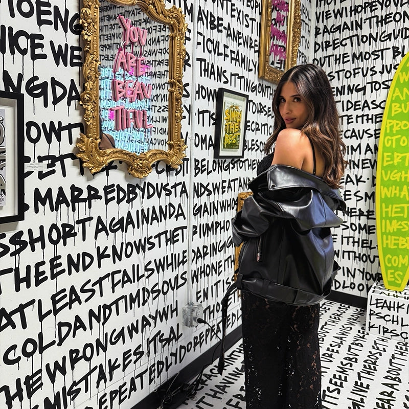 Visitor in Gallery DeFi’s black-and-white writing room, with a gold-framed mirror and green surfboard.